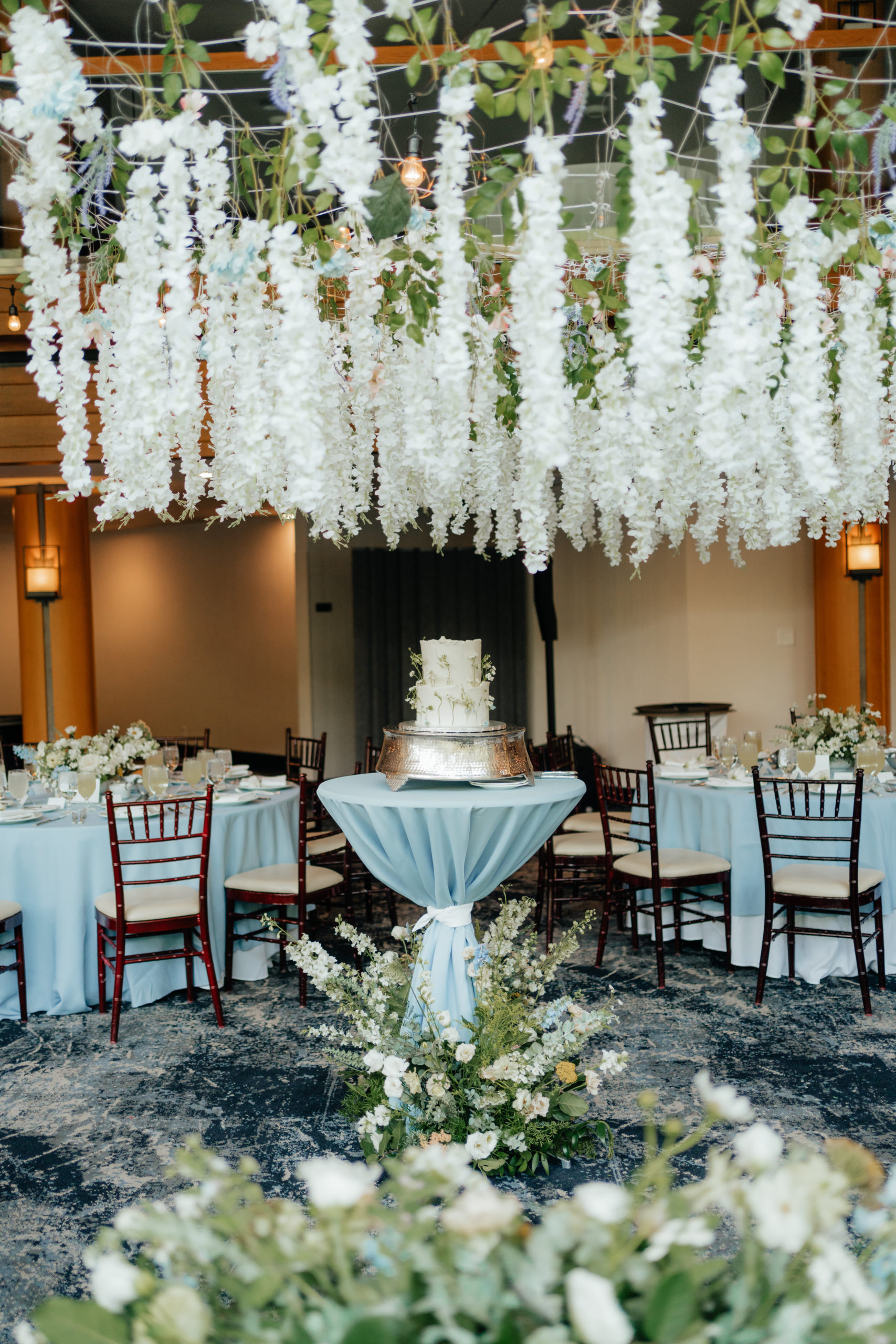 Wildflower wedding florals hanging from a ceiling and detailing a cake in the center of the room.